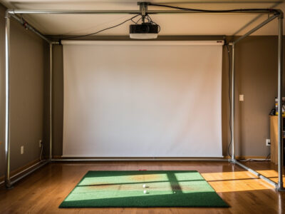 DIY golf simulator enclosure with EMT conduit frame and impact screen in a home room