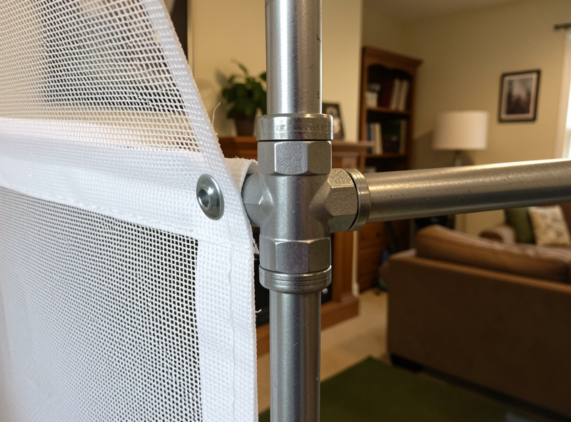 DIY golf simulator enclosure with EMT conduit frame and tensioned impact screen in a home room