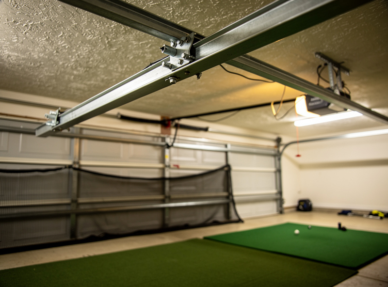 Garage interior showing the door track and opener rail hanging into the ceiling space above a golf hitting area
