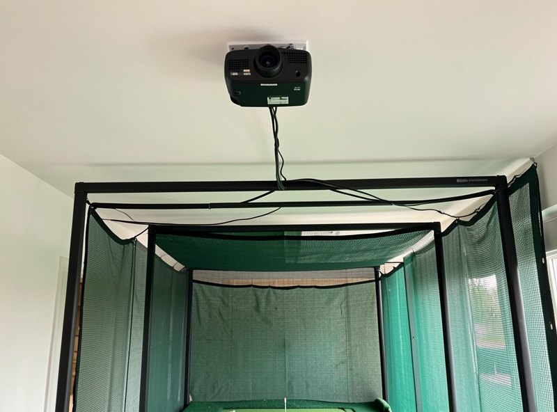 Tidy cable run and power feed to a ceiling-mounted projector above a home golf simulator enclosure