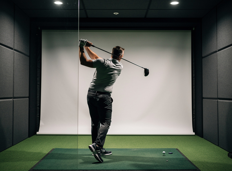 Golfer at the top of the backswing showing lateral clearance to the side wall inside a simulator enclosure